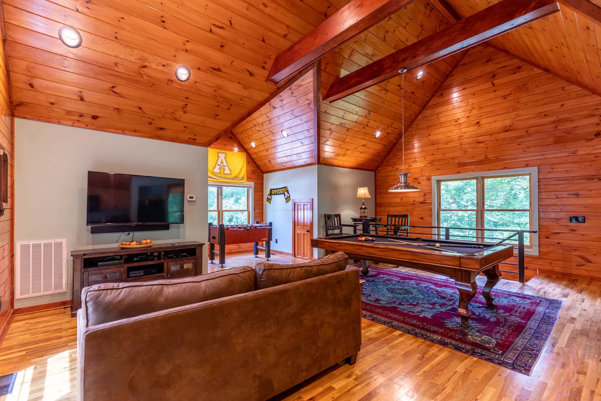 An inviting entertainment area showcasing a pool table, sofa, large windows allowing natural light, and a television. The space feels open and comfortable, ideal for both active play and relaxing with family or friends.