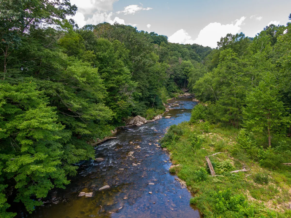 A serene, scenic view of the flowing river bordered by lush greenery and natural rock formations. The peaceful setting invites fishing, hiking, wildlife spotting, or simply relaxing by the water—embodying the spirit of outdoor adventure highlighted in the section.