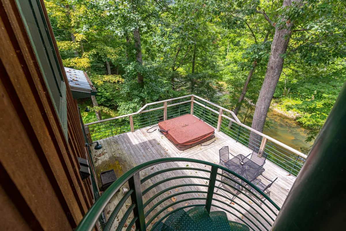 A wooden deck featuring a hot tub, surrounded by trees and outdoor seating. The scene is peaceful, hinting at views of the river and the perfect spot for morning coffee or evening unwinding.