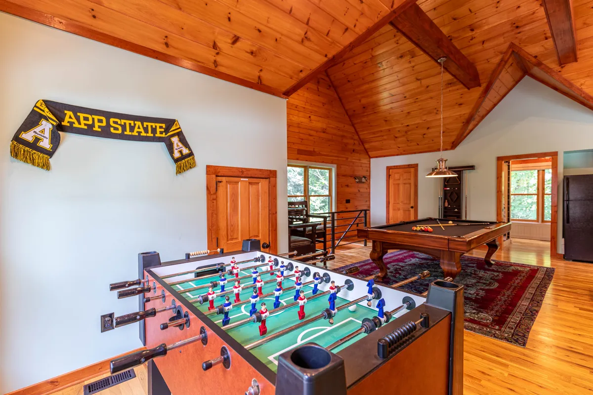 A lively game area featuring both a foosball table and pool table, complete with a wooden ceiling and a collegiate banner on the wall. The setup encourages group play and friendly competition, reflecting an energetic and youthful vibe.