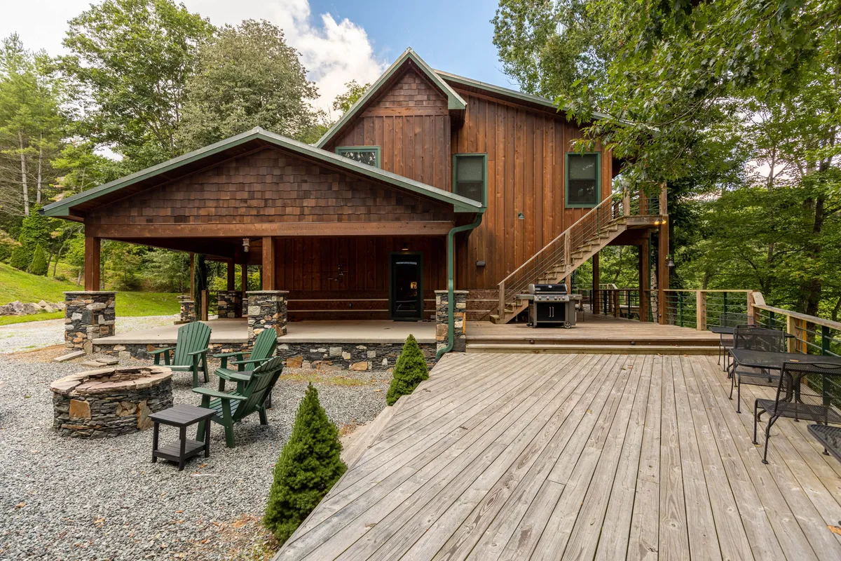 The exterior shot features a wooden house with a fire pit, a spacious deck, and stairs leading to an upper level. The scene evokes a sense of togetherness, with inviting spaces for gathering, barbecuing, relaxing by the fire, and enjoying starlit evenings.