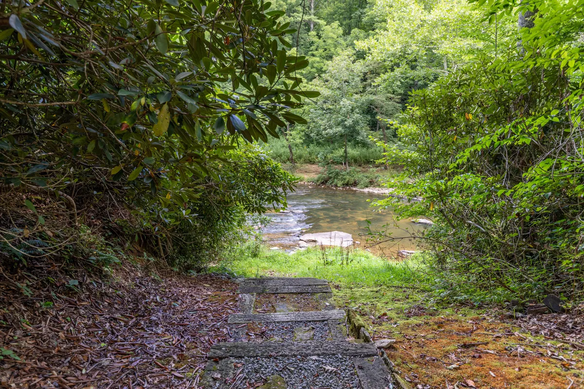 A serene riverside scene with stone steps leading down to a river, surrounded by lush greenery. The area invites moments of quiet reflection as well as active adventures, such as hiking and exploring along the riverbanks.