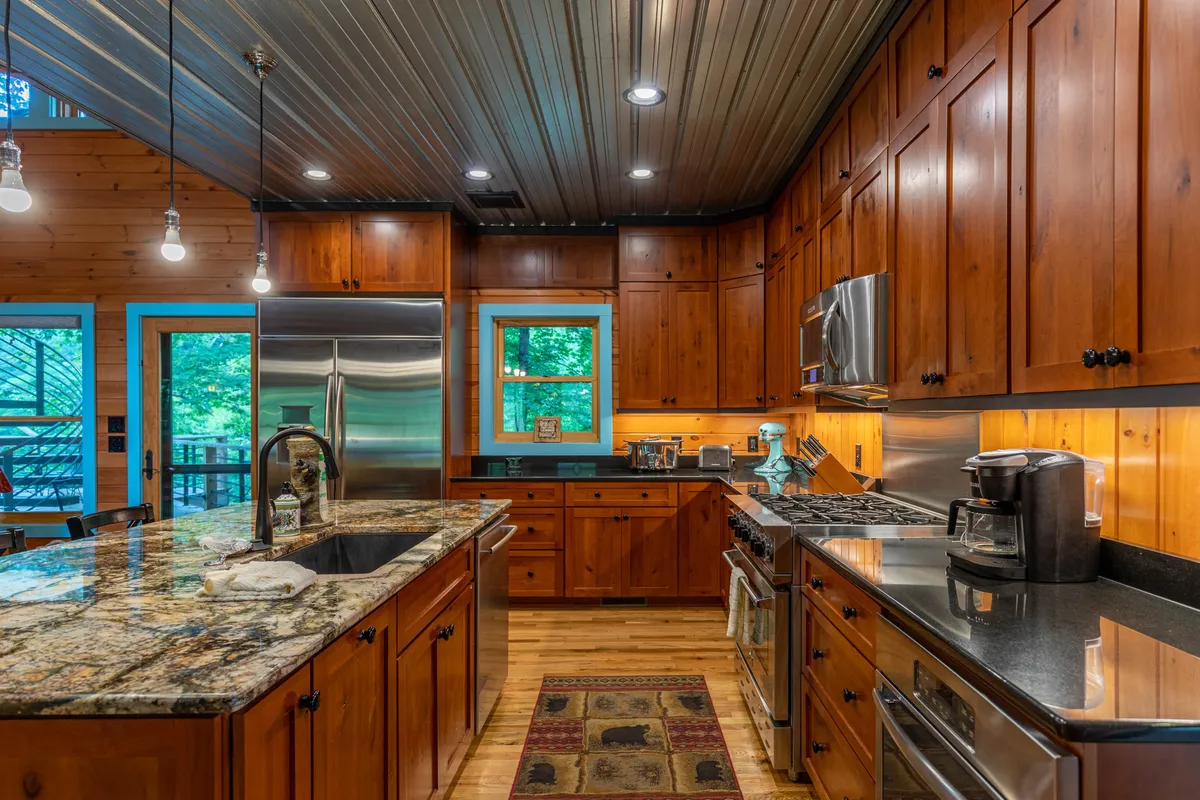 A close-up view of the gourmet kitchen featuring granite countertops, stainless steel high-end appliances, and wooden cabinets. The kitchen island and ample windows make the space perfect for both cooking and casual dining.